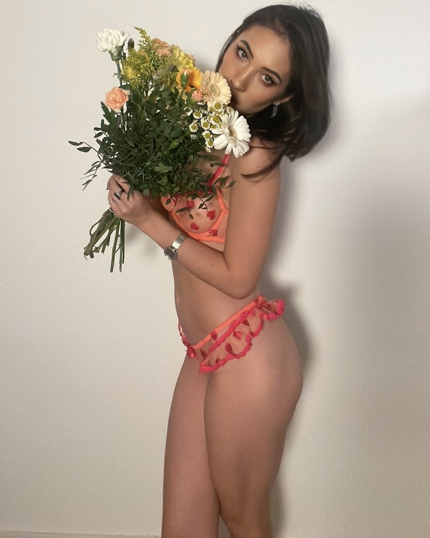Alice in coral lingerie, holding a bouquet of flowers